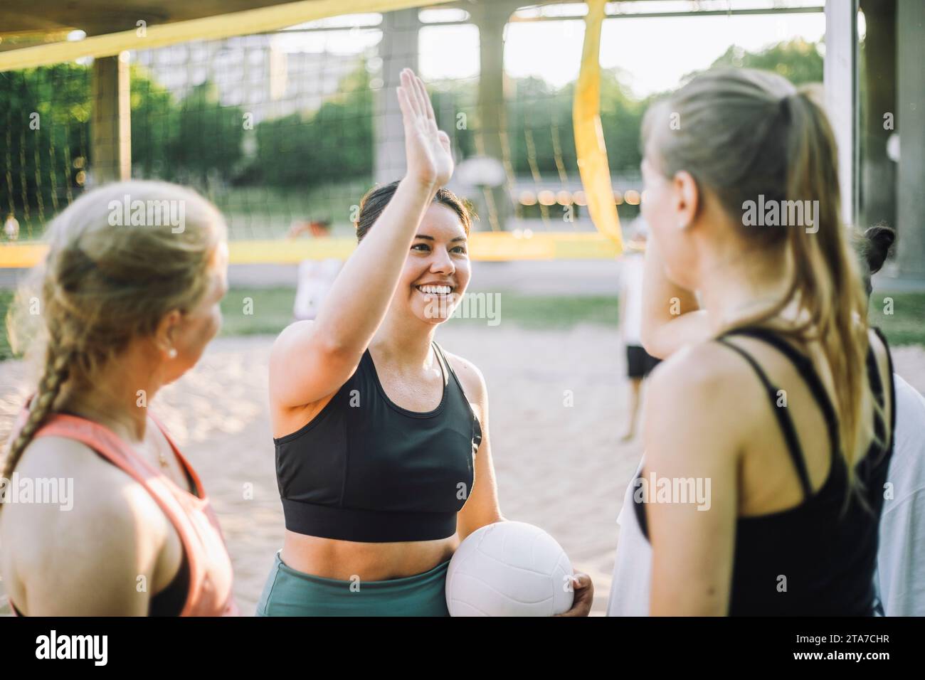 Donna sorridente che regala cinque premi a un'amica mentre gioca a pallavolo Foto Stock