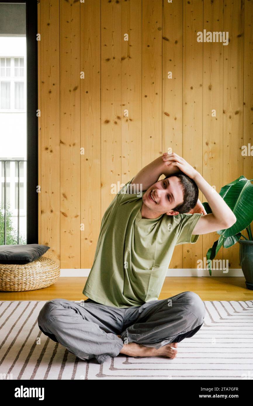 Uomo sorridente che si allena mentre si siede a casa con le gambe incrociate Foto Stock