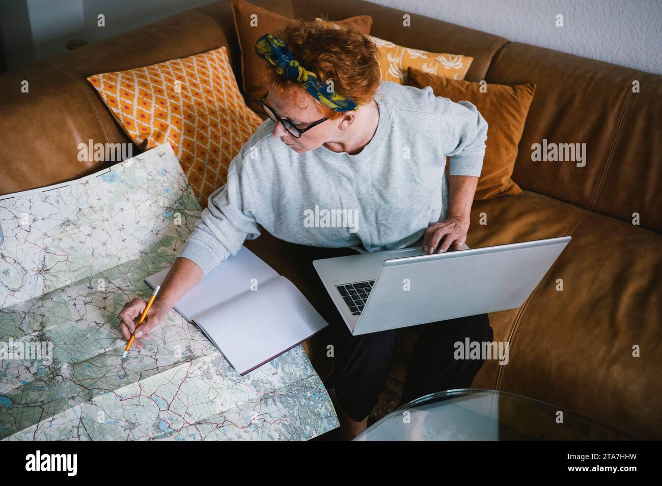 Vista laterale di una donna anziana che pianifica un viaggio sulla mappa e utilizza il computer portatile a casa Foto Stock