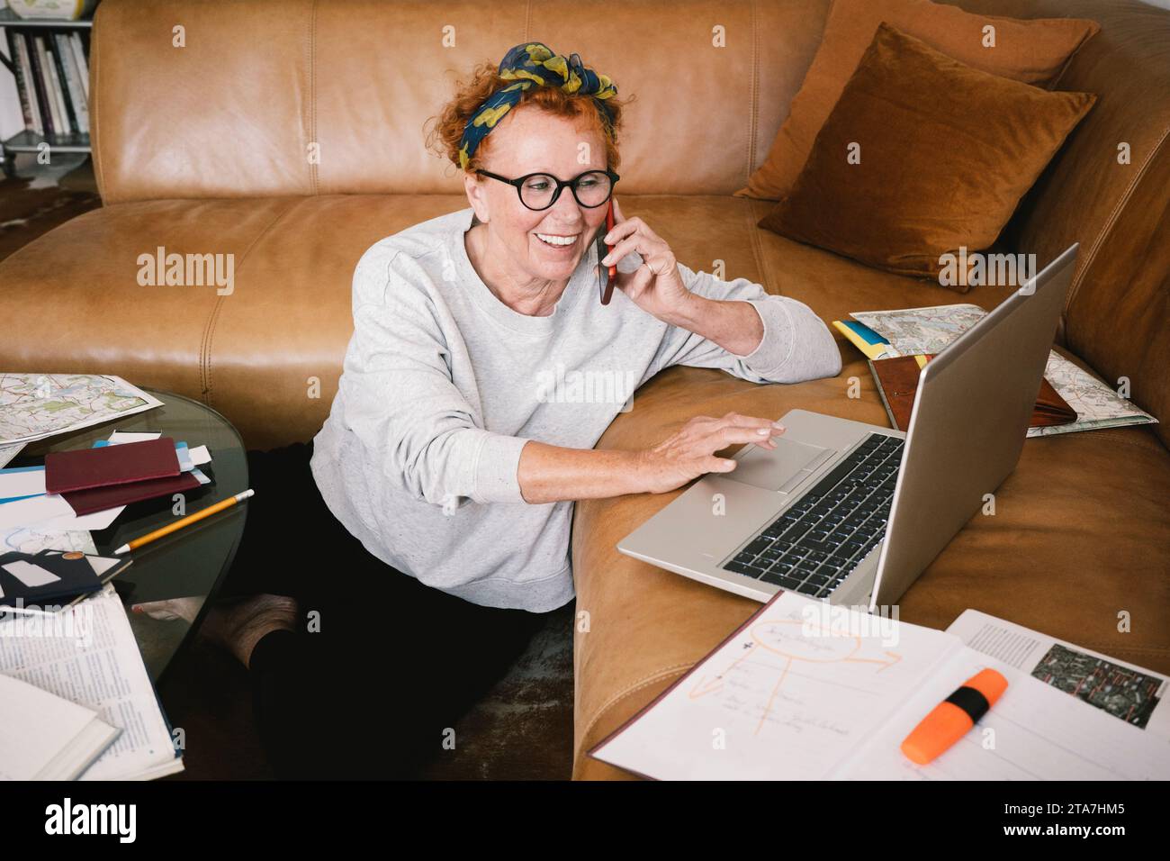 Donna anziana felice che parla al telefono cellulare e usa il computer portatile a casa Foto Stock