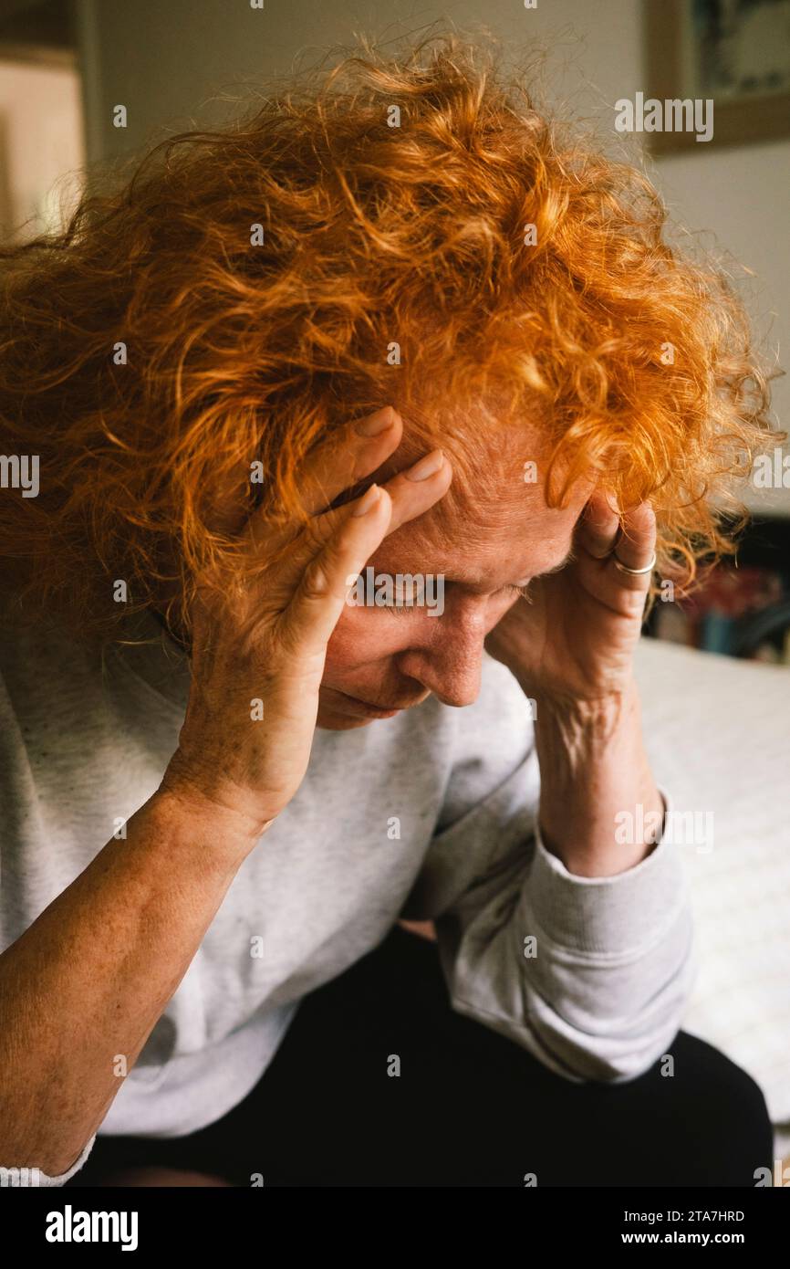 Depresso rossa anziana donna seduta con la testa nelle mani sul letto Foto Stock