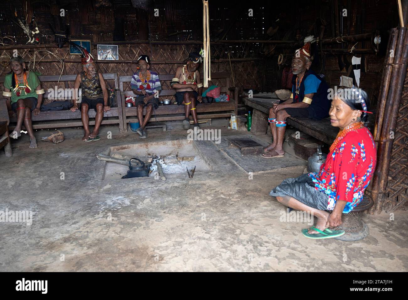 Gli anziani della tribù Konyak e la moglie dei re seduti in una casa tradizionale, guerrieri con splendidi ornamenti tribali e tatuaggi facciali, Nagaland, India Foto Stock
