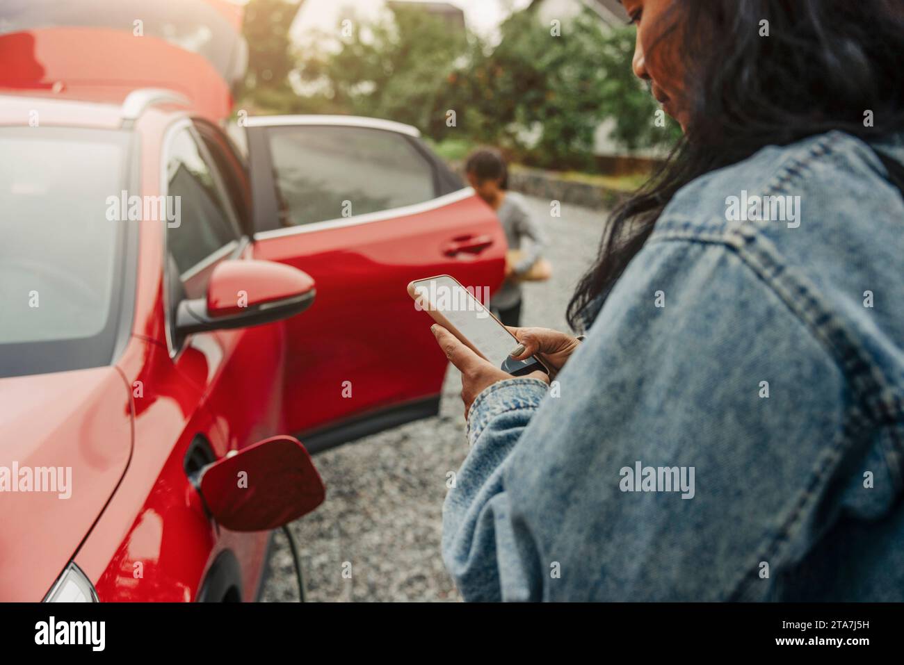 Donna che usa uno smartphone vicino all'auto elettrica Foto Stock
