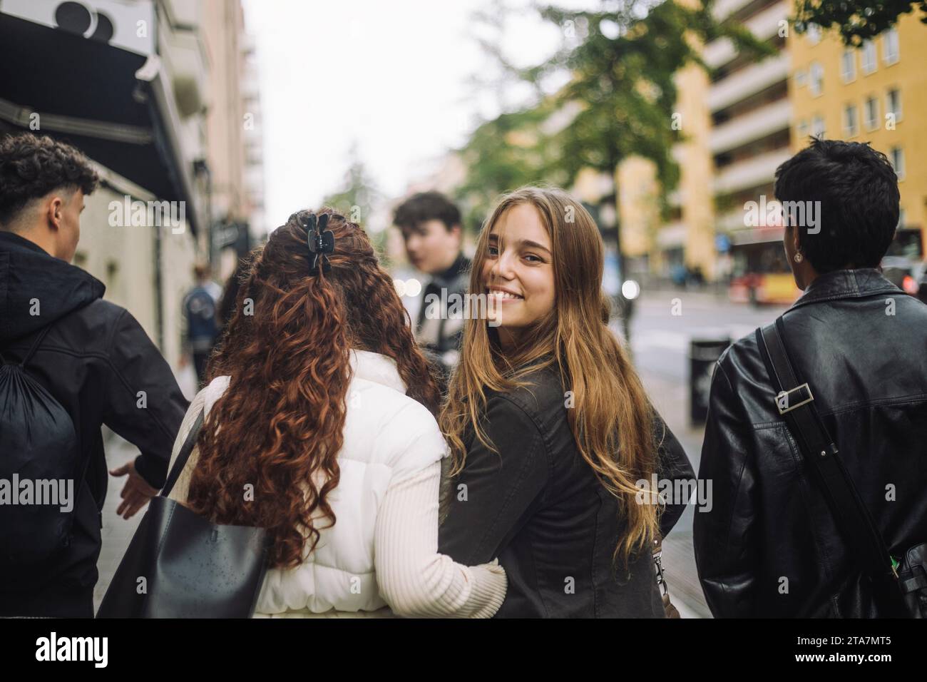Ritratto di una ragazza sorridente che guarda alle spalle mentre cammina con gli amici in strada Foto Stock