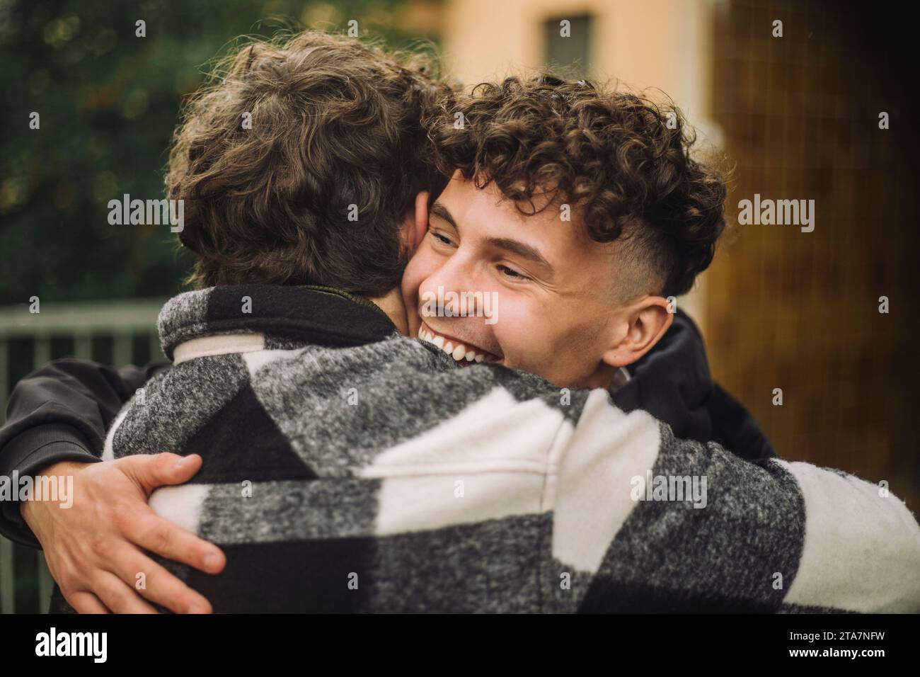 Ragazzo felice con i capelli ricci che abbraccia un amico maschio che indossa una camicia in flanella Foto Stock