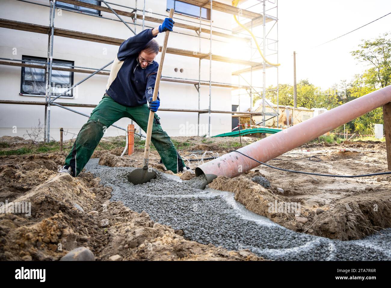 Uomo che distribuisce calcestruzzo fresco per la fondazione di un edificio Foto Stock