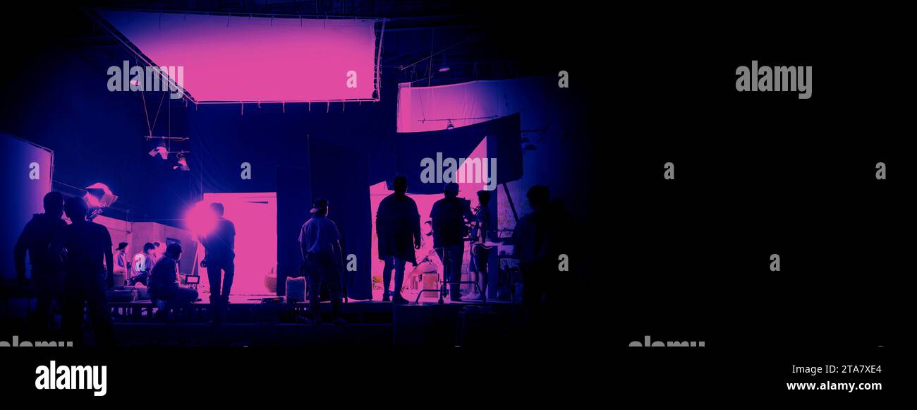 Silhouette di persone che lavorano in un grande studio di produzione per la ripresa o la registrazione di video cinematografici con fotocamera digitale e set di illuminazione. Foto Stock