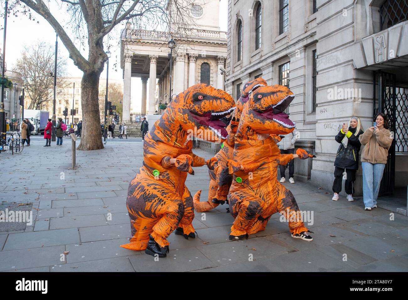 Londra, Regno Unito. 28 novembre 2023. I Dancing Dinasours si esibivano oggi a Londra da Trafalgar Square. Potrebbero essere stati ballerini del musical del West End The Lion King. I manifestanti anti anti Ultra Low Emission zone sono stati visti anche a Londra in alcune occasioni, vestiti da dinasours che bloccano i furgoni fotografici ULEZ mobili che scattano immagini di auto nelle aree ULEZ. Credito: Maureen McLean/Alamy Live News Foto Stock