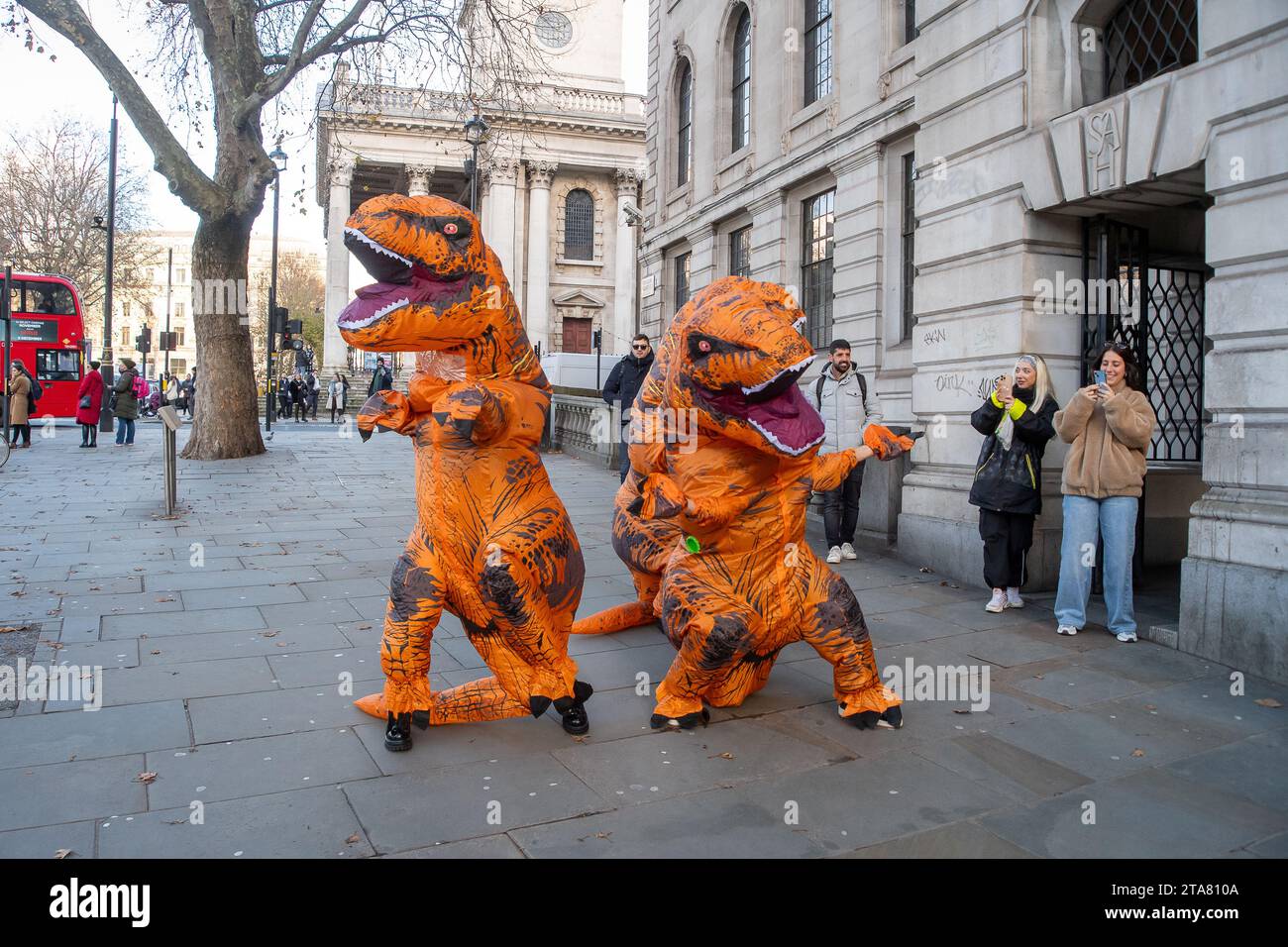 Londra, Regno Unito. 28 novembre 2023. I Dancing Dinasours si esibivano oggi a Londra da Trafalgar Square. Potrebbero essere stati ballerini del musical del West End The Lion King. I manifestanti anti anti Ultra Low Emission zone sono stati visti anche a Londra in alcune occasioni, vestiti da dinasours che bloccano i furgoni fotografici ULEZ mobili che scattano immagini di auto nelle aree ULEZ. Credito: Maureen McLean/Alamy Live News Foto Stock