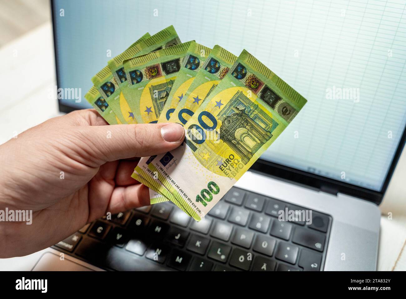 24 novembre 2023: Un uomo detiene diverse banconote in euro da 100 davanti al suo computer portatile *** Ein Mann hält mehrere 100 Euro Geldscheine vor seinem laptop Foto Stock
