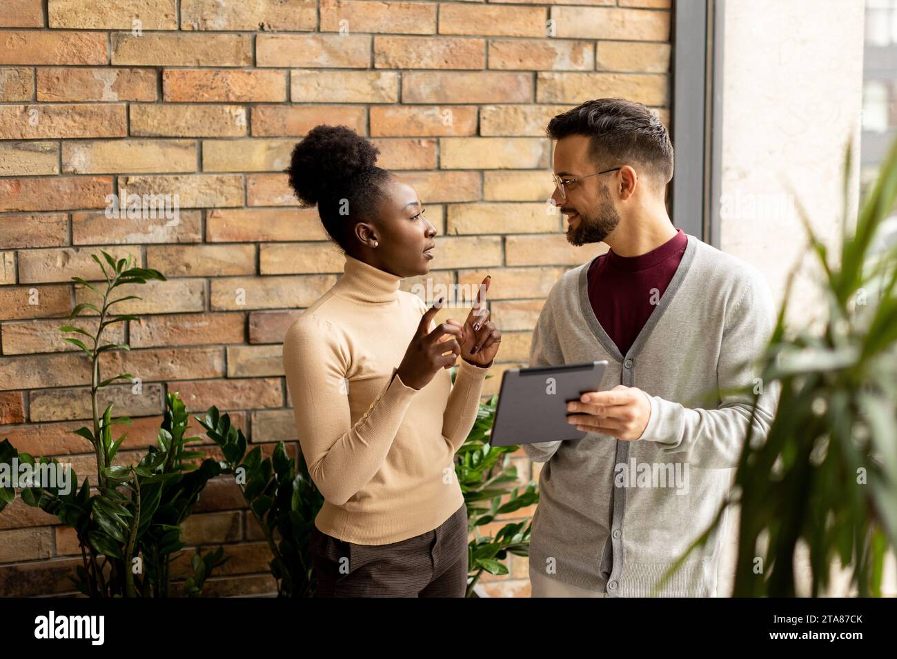 Bella giovane coppia di aziende multietniche con tablet digitali in piedi e discutere in un ufficio moderno Foto Stock