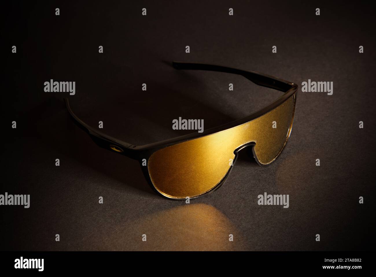 Una fantastica foto in studio di un paio di occhiali da sole sportivi Oakley con lenti dorate, su uno sfondo nero scuro Foto Stock
