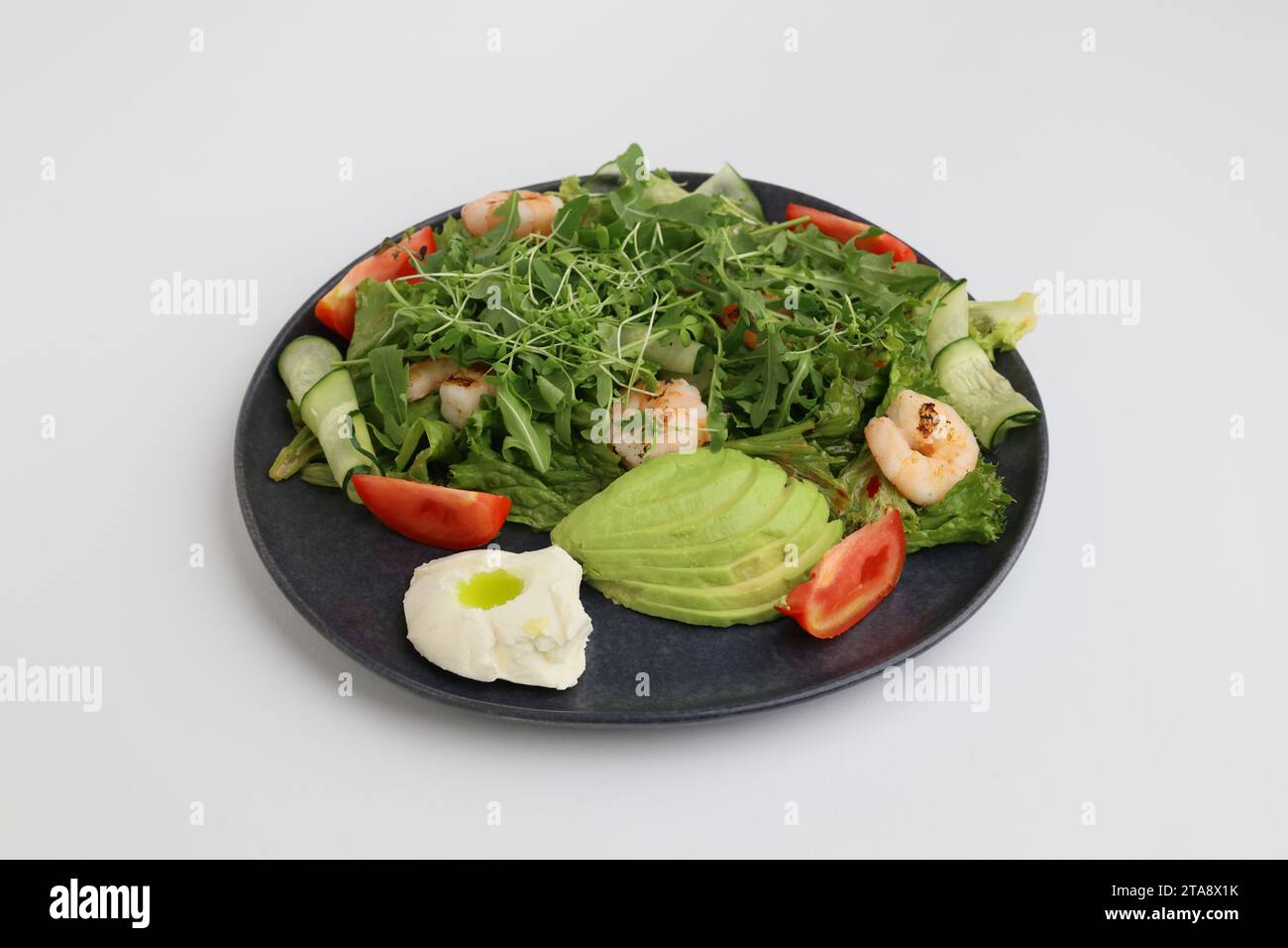 Insalata di gamberi, avocado, lattuga e pomodori ciliegini. Gustose foglie miste di verdure con gamberi grigliati in piatto nero su sfondo bianco. Foto Stock