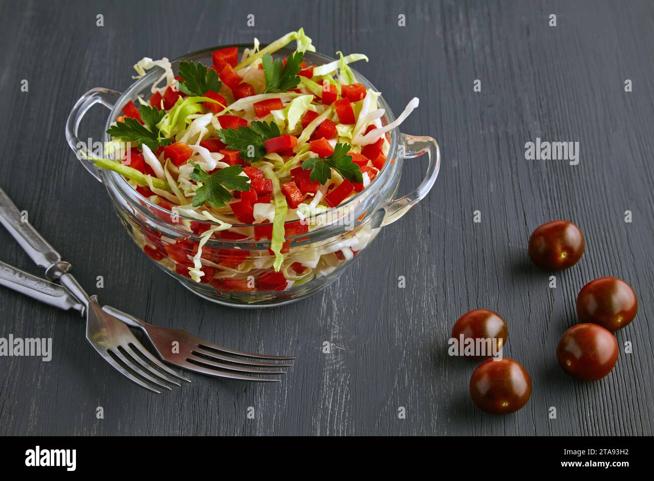 Insalata di verdure leggere di cavolo e peperoni in una ciotola di vetro e posate su un tavolo di legno nero. Foto Stock