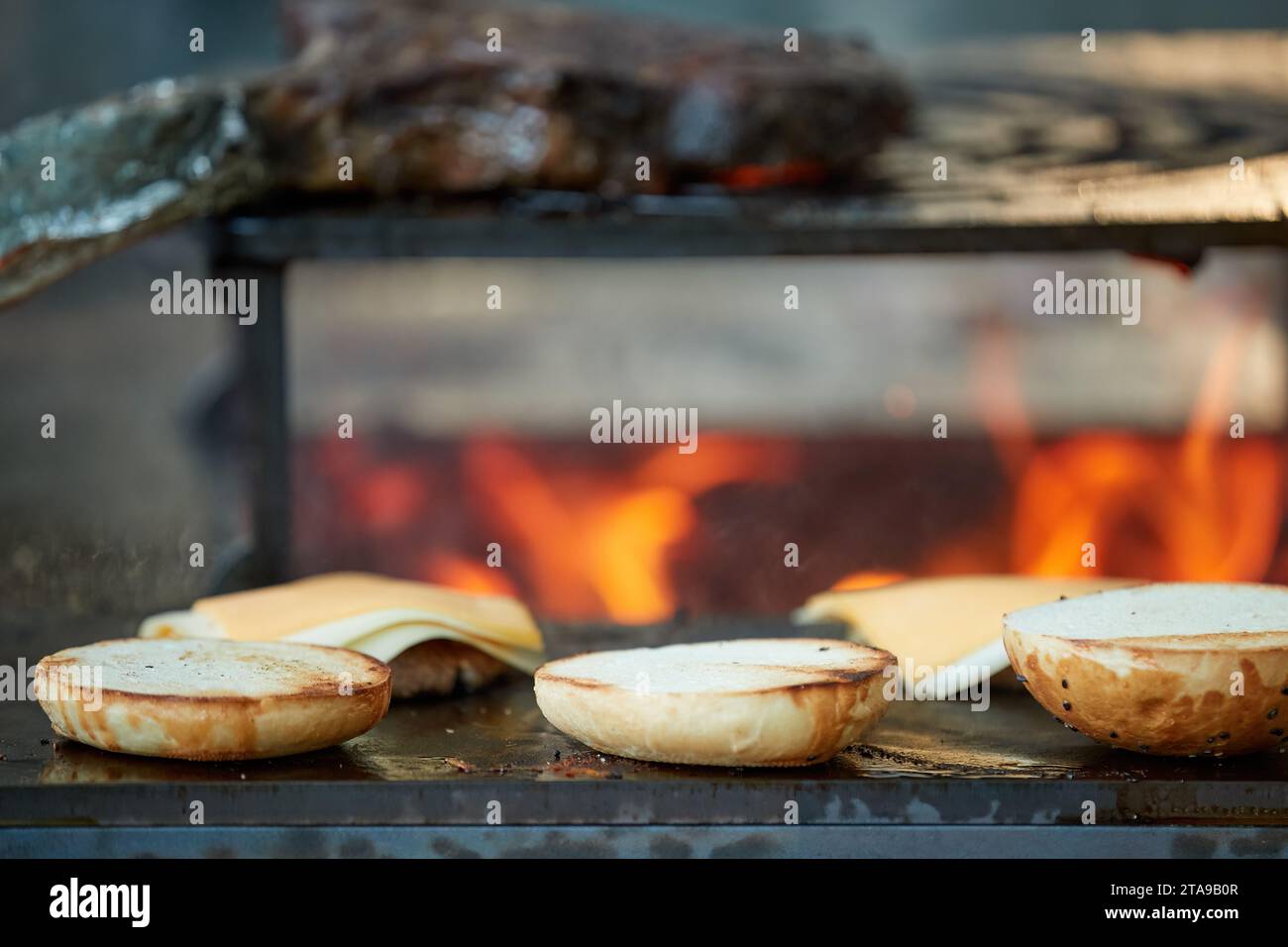 Uno chef prepara hamburger su una griglia all'aperto. Primo piano della cucina al festival del giardino, fiamme, profondità di campo bassa, sfondo sfocato molto colorato, Foto Stock