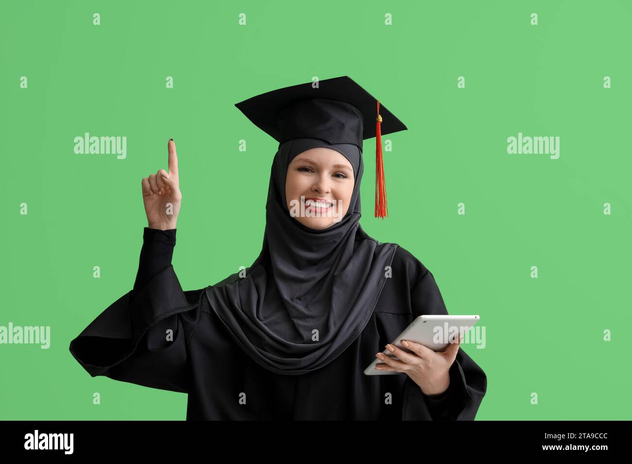 Studente laureato musulmano con un tablet che punta a qualcosa su sfondo verde Foto Stock