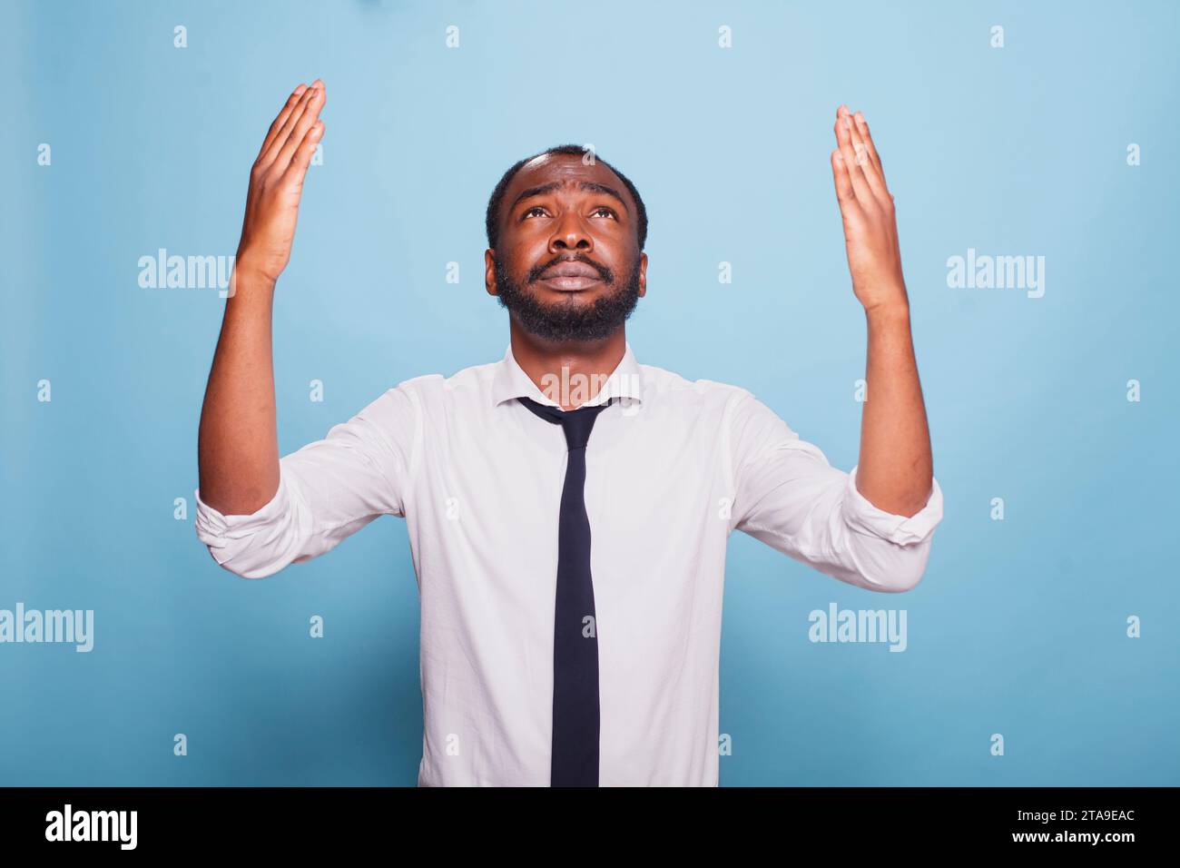 Un uomo d'affari nero preoccupato sta pregando e alzando le mani con un umile gesto verso il cielo. Un dipendente afroamericano che indossa una cravatta nera e una camicia bianca chiede perdono Foto Stock