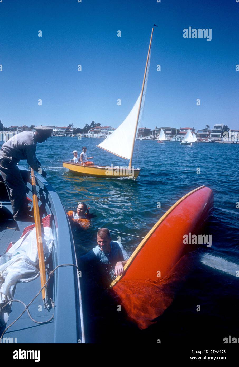 NEWPORT BEACH, CA - MAGGIO 1956: Una giovane coppia nuota in sicurezza dopo che la loro barca a vela è stata rovesciata nel porto intorno al maggio 1956 al Newport Yacht Club di Newport Beach, California. (Foto di Hy Peskin) Foto Stock