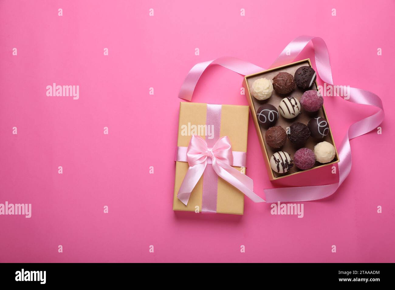 Scatola aperta con deliziose caramelle di cioccolato e nastro su sfondo rosa, vista dall'alto. Spazio per il testo Foto Stock