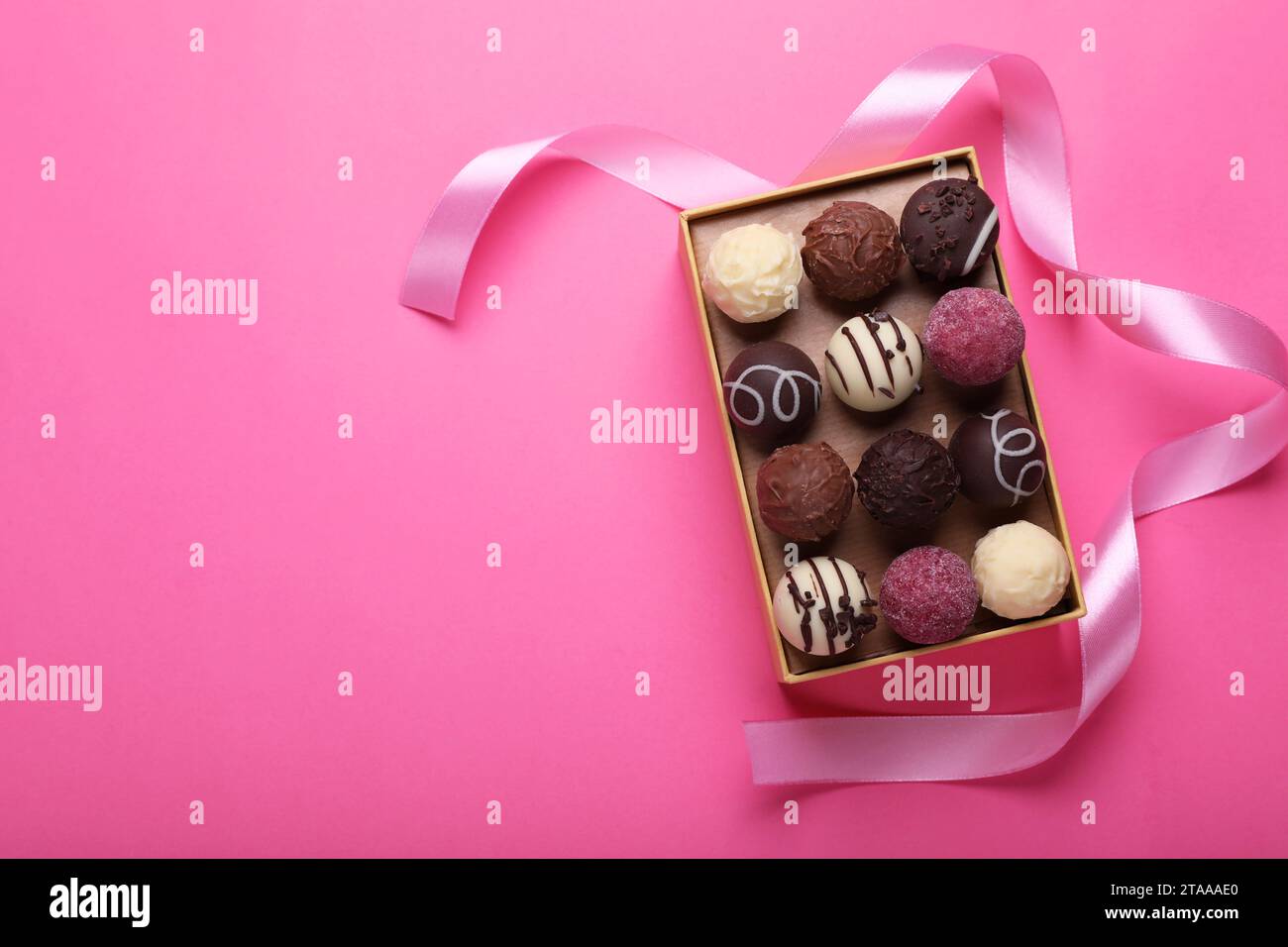 Scatola aperta con deliziose caramelle di cioccolato e nastro su sfondo rosa, vista dall'alto. Spazio per il testo Foto Stock