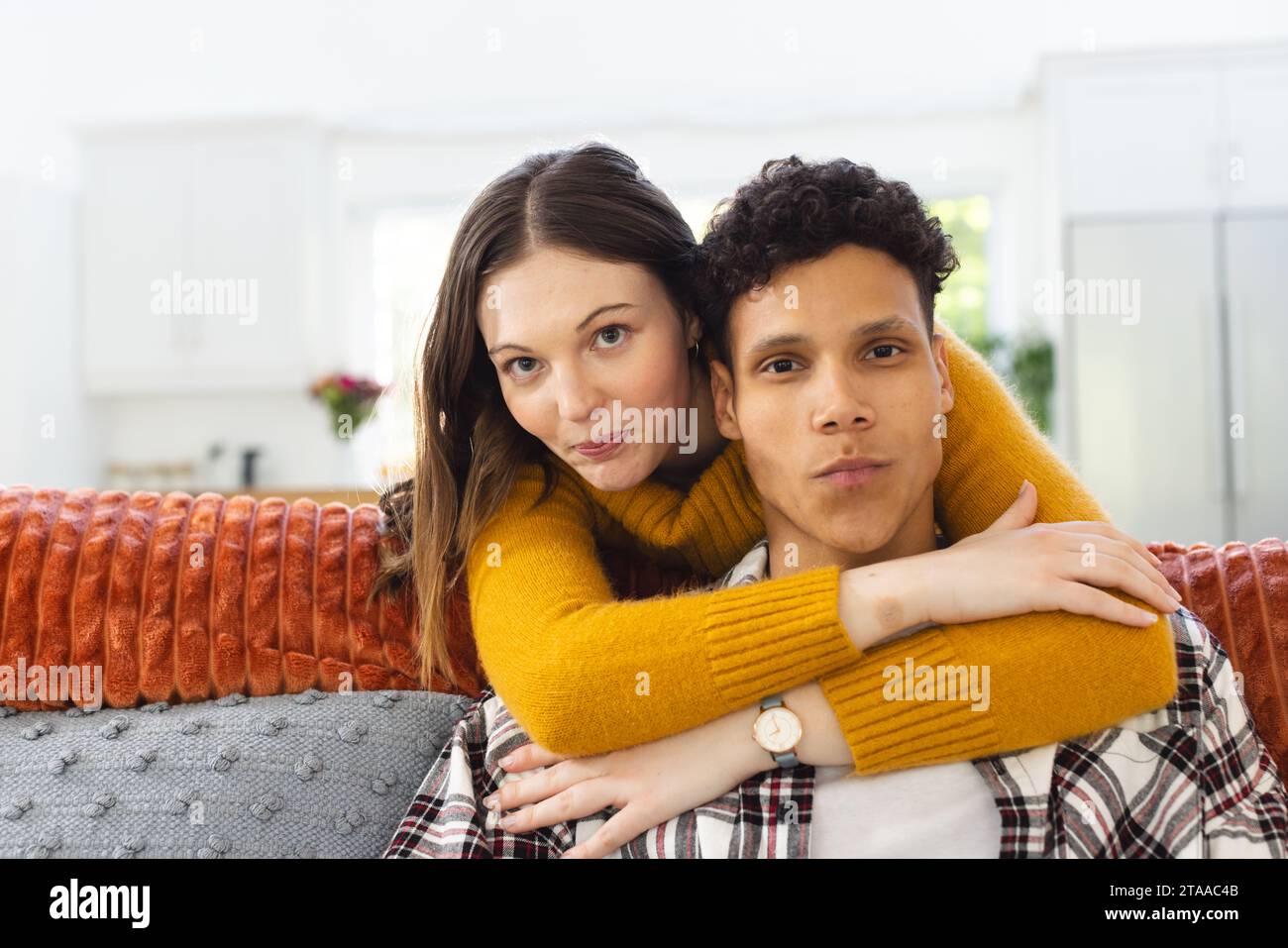 Ritratto di una coppia felice e diversificata che si abbraccia sul divano a casa, spazio copia. Espressione, tempo libero, amore, insieme, gesticolazione, divertimento e vita domestica Foto Stock