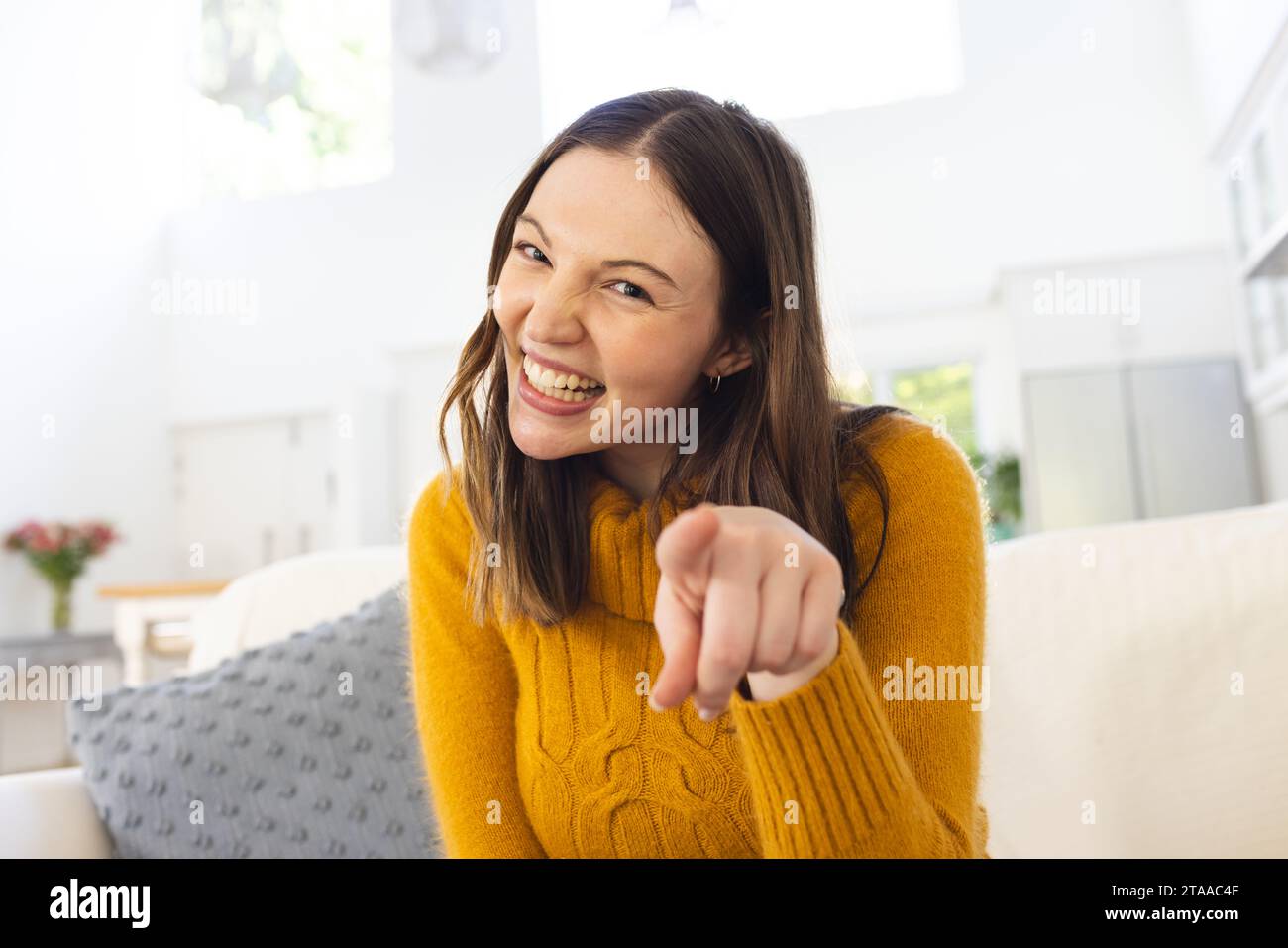 Ritratto di una donna caucasica felice seduta sul divano e puntata con il dito a casa, spazio copia. Espressione, tempo libero, gesticolazione, direzione e dom Foto Stock
