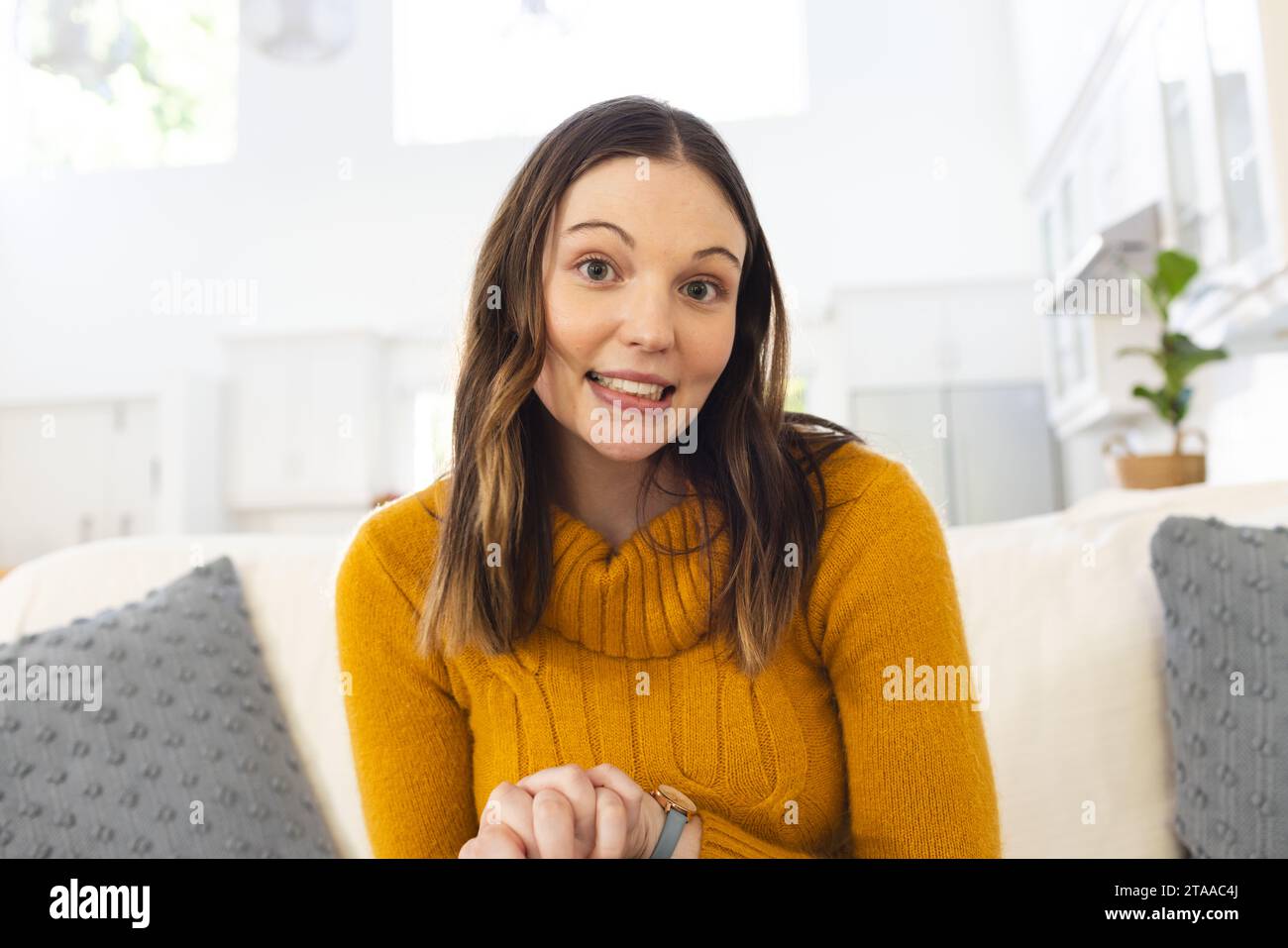 Ritratto di una donna caucasica felice seduta sul divano, che si tiene per mano a casa, copia spazio. Espressione, tempo libero, gesticolazione e vita domestica inalterati. Foto Stock