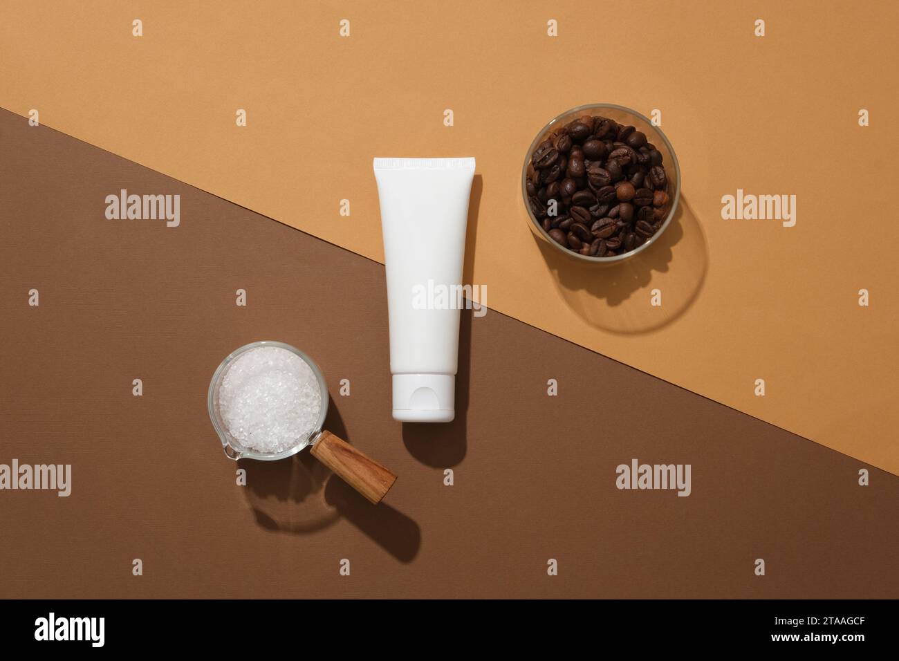 Scena minimalista per pubblicizzare cosmetici con ingredienti naturali. Vista dall'alto di un tubo di plastica bianco senza etichetta decorato con una tazza di vetro di chicchi di caffè Foto Stock