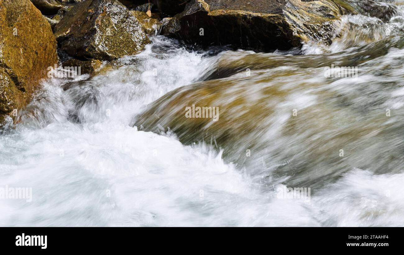 L'acqua si sfuoca dalle striature d'acqua al caos che schiude contro grandi rocce Foto Stock