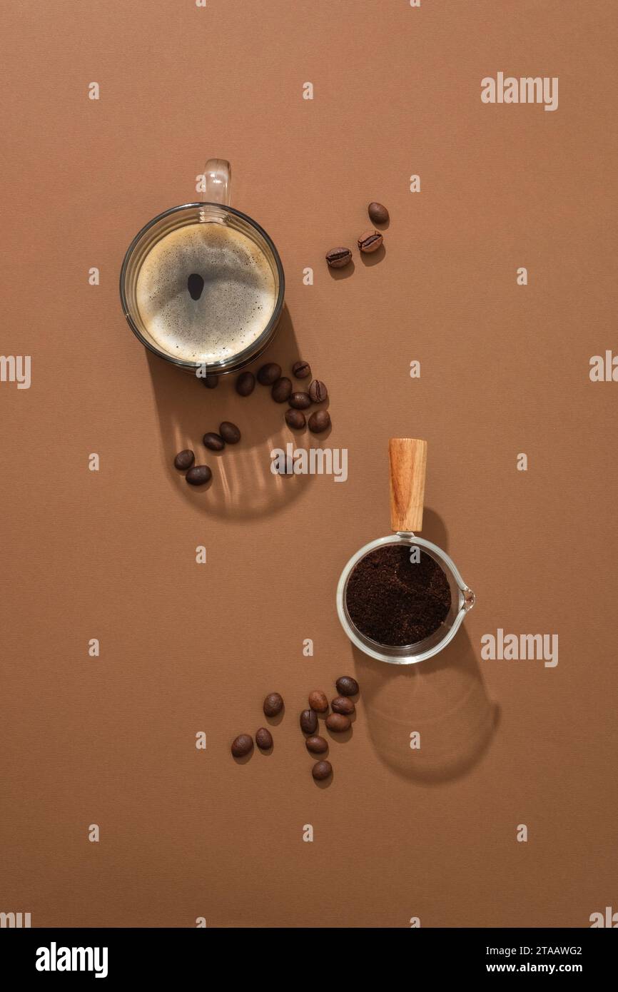 Vista dall'alto di una tazza di caffè con chicchi di caffè e vassoio di caffè in polvere su sfondo marrone. Scena minimalista per pubblicizzare una bevanda a base di caffè Foto Stock