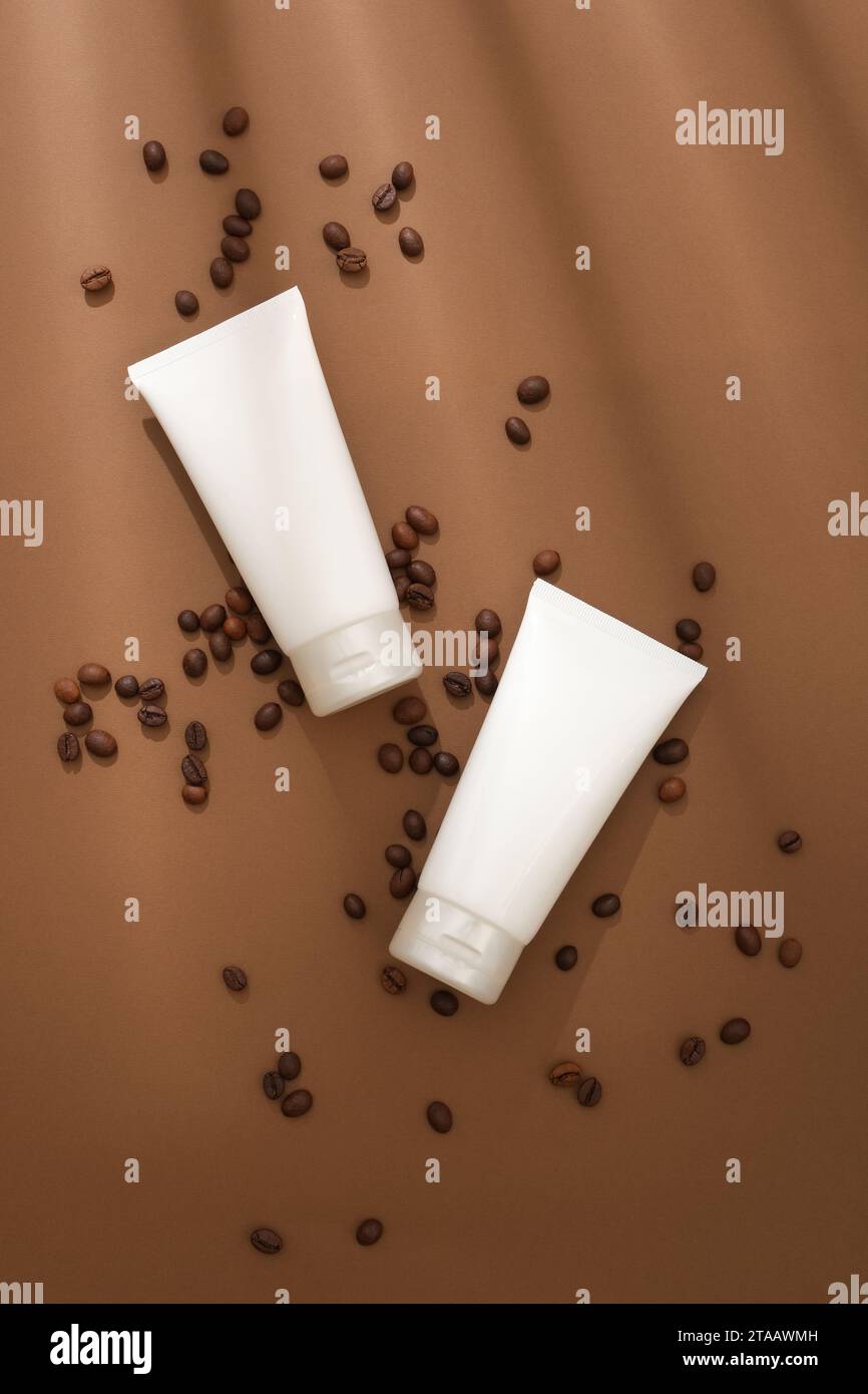 Tubo di plastica bianco con crema idratante per il viso o detergente per il viso visualizzato su sfondo marrone con chicchi di caffè. Scena minimalista per la pubblicità Foto Stock