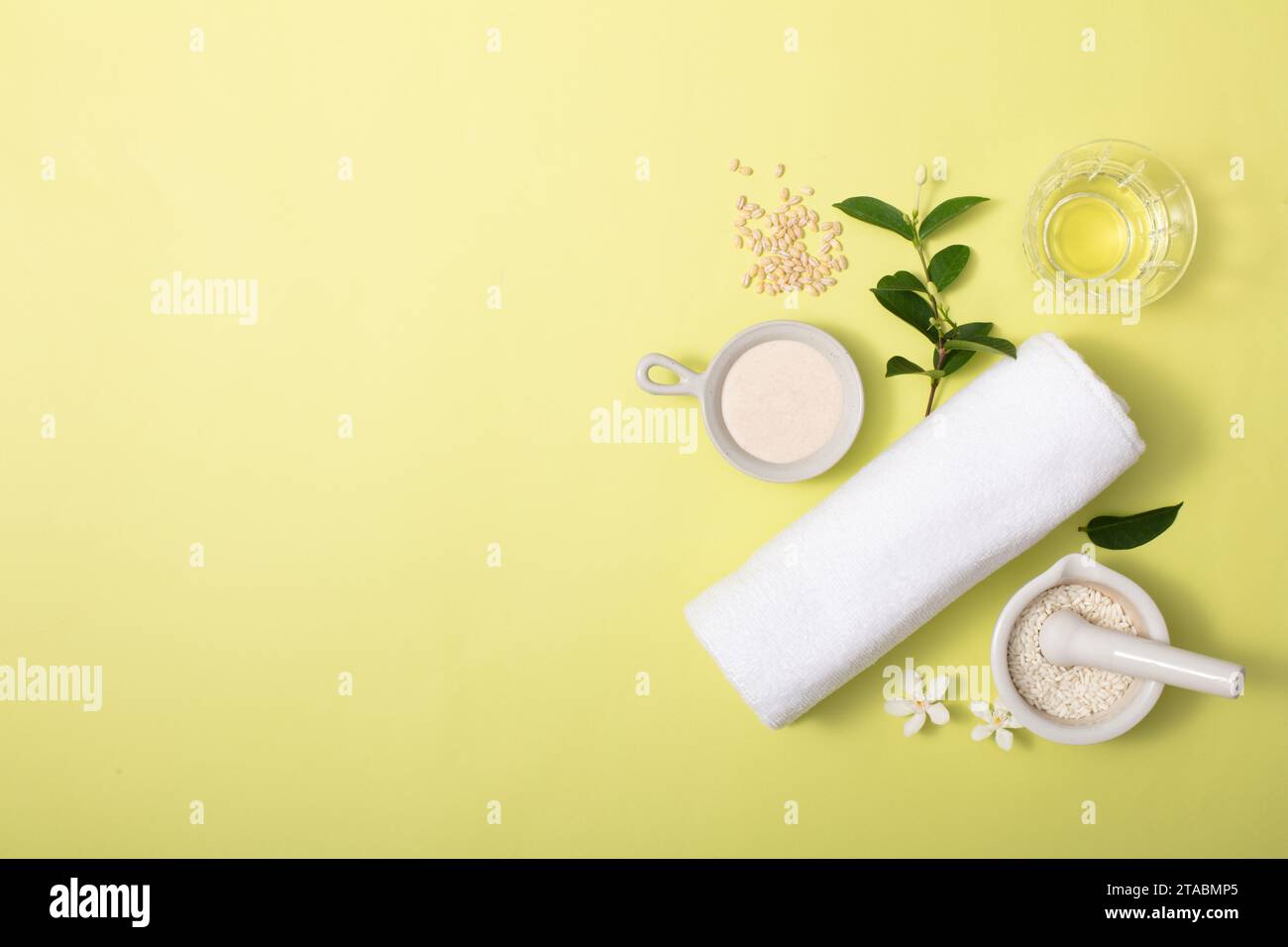 La polvere di crusca di riso è contenuta in utensili di ceramica, foglie verdi, un bicchiere e un asciugamano su sfondo giallo chiaro. Spazio libero per il design o il prodotto di Foto Stock