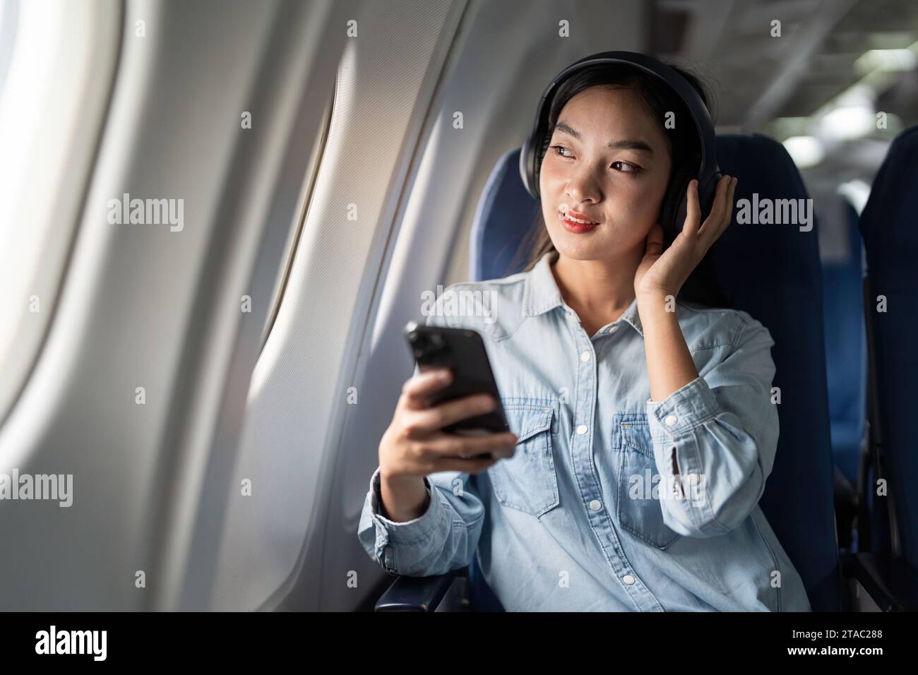 Giovane donna che ascolta la canzone durante il volo in cabina di prima classe utilizzando lo smartphone, la donna si diverte a bordo dell'aereo e ascolta la musica con le cuffie Foto Stock