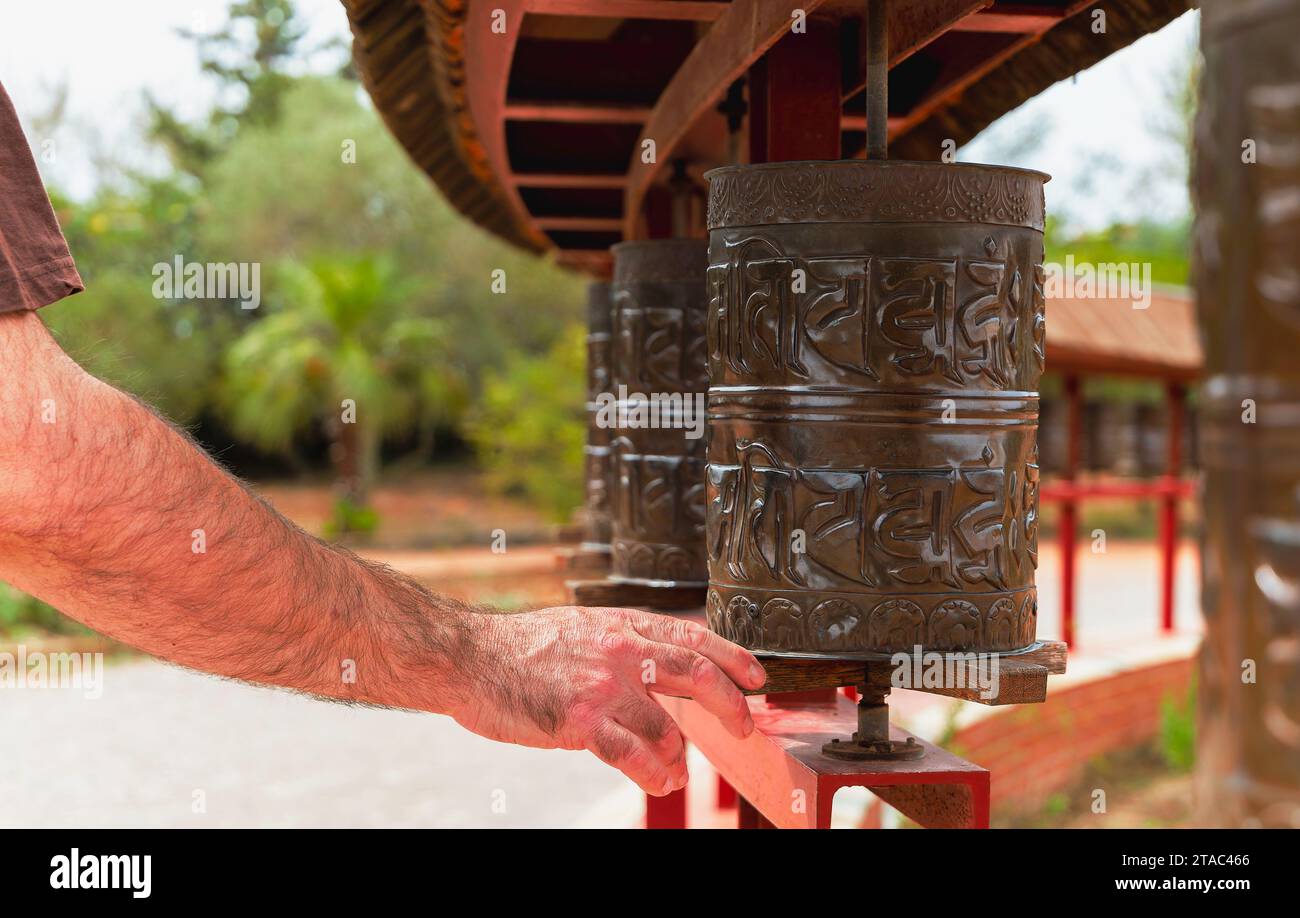 La mano di un uomo che gira una ruota di preghiera buddista, scolpita con mantra. Tempio buddista di El Garraf Sakya Tashi Ling, Barcellona, Spagna. Un simbolo di spiri Foto Stock