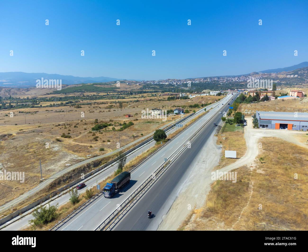 Vista dall'alto di una strada asfaltata con automobili, campi, montagne vicino alla città in una giornata di sole, la Turchia. Foto Stock