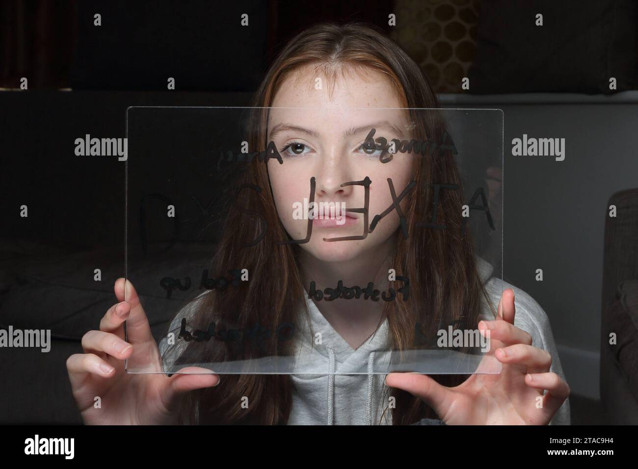 La ragazza adolescente tiene una tavola di plastica trasparente con parole relative alla dislessia davanti al viso, mostrando emozioni Foto Stock