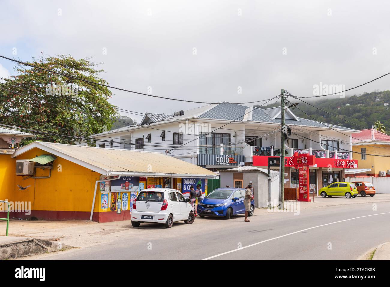 Anse Royale, Seychelles - 18 agosto 2023: Vista sulla strada con automobili e piccoli negozi lungo la strada, gente del posto cammina per la strada Foto Stock