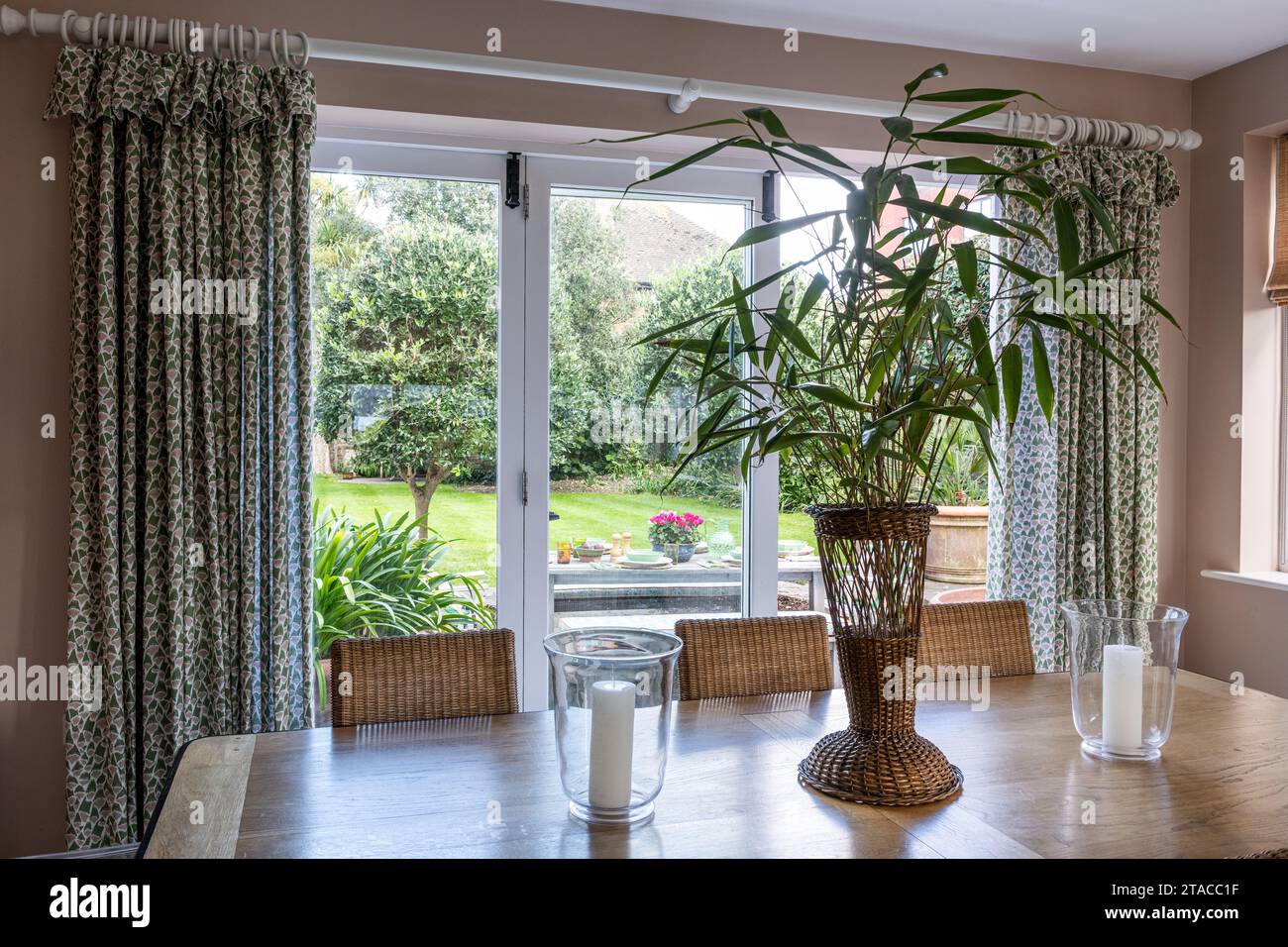 Bambù in vaso di vimini sul tavolo con vista giardino. Casa in stile Arts and Crafts degli anni '1930. Hove, East Sussex, Regno Unito. Foto Stock