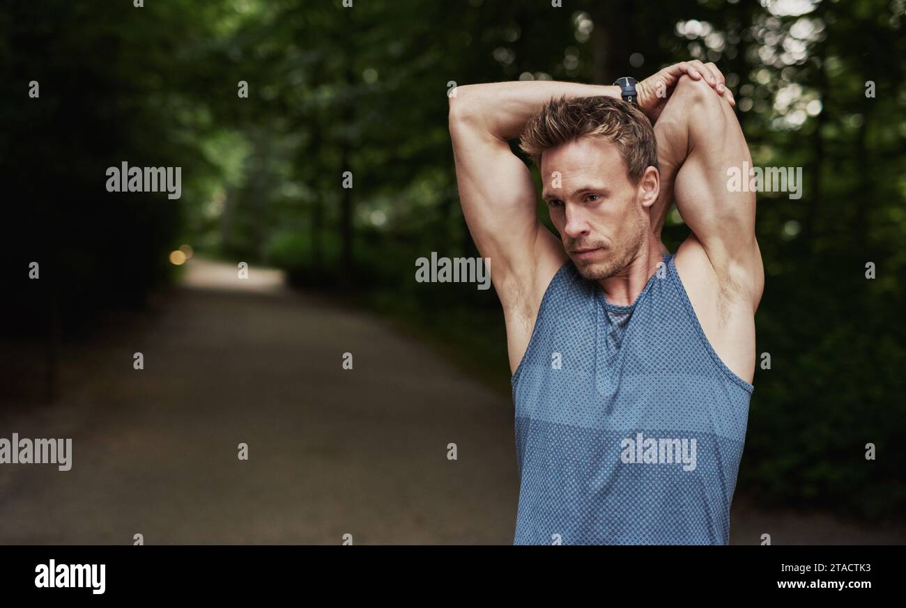 Immagine a mezzo corpo di un giovane atletico che si allunga le braccia dietro la testa mentre si allena in un allenamento fitness all'aperto. Foto Stock