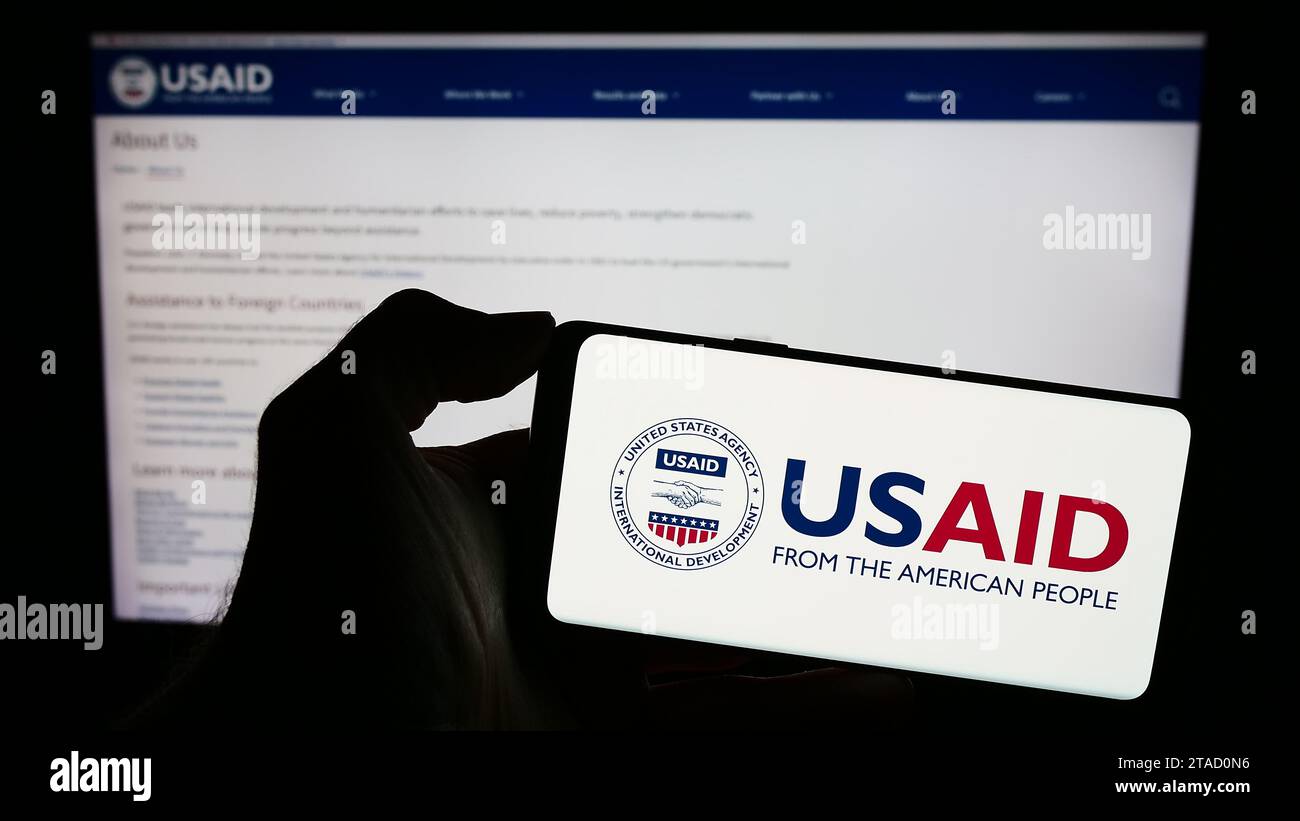 Persona in possesso di un cellulare con il logo della United States Agency for International Development (USAID) davanti alla pagina web. Concentrarsi sul display del telefono. Foto Stock