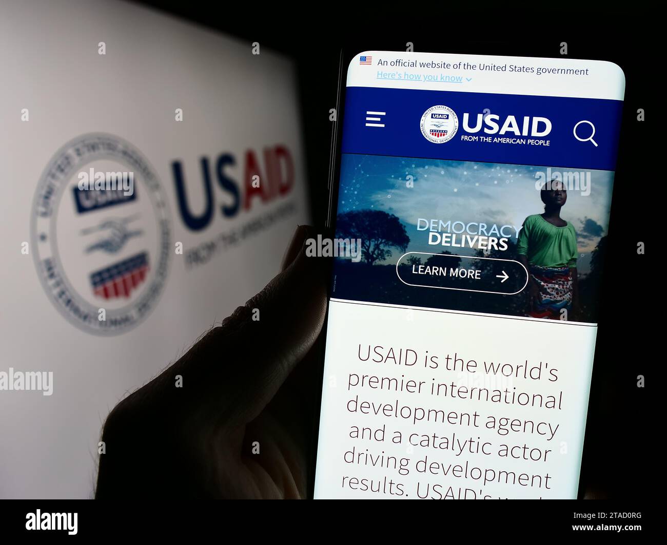 Persona in possesso di un cellulare con pagina Web dell'Agenzia degli Stati Uniti per lo sviluppo internazionale (USAID) con logo. Concentrarsi sul centro del display del telefono. Foto Stock