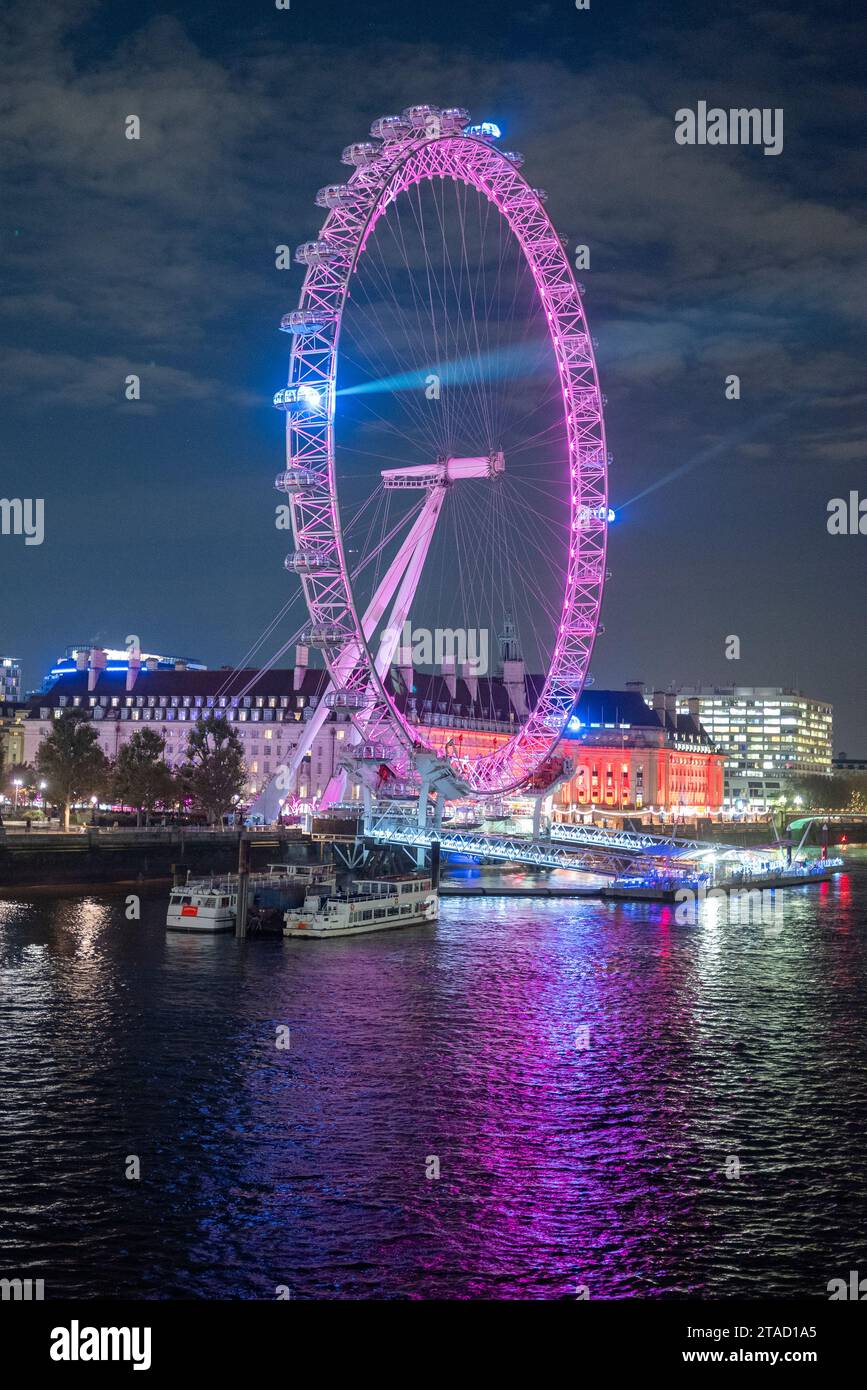 Luci laser che emettono da un London Eye viola in un cielo notturno con riflessi nel Tamigi, Londra, novembre 2023 Foto Stock