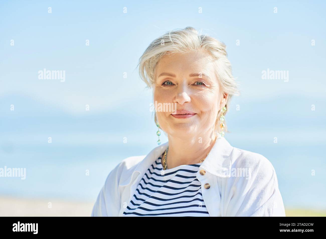 Ritratto di primo piano estivo all'aperto di una donna matura felice e sana di 50 - 55 anni che si gode una bella giornata di sole in riva al lago o al mare, stile di vita attivo Foto Stock