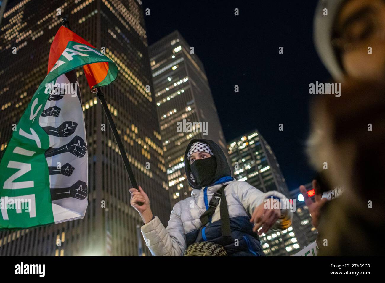 NEW YORK, NEW YORK - NOVEMBRE 29: Un giovane sostenitore pro-palestinese seduto sulle spalle regge una bandiera palestinese durante una manifestazione all'edificio News Corp. Vicino all'illuminazione dell'albero Rockefeller il 29 novembre 2023 a New York. Il raduno arriva quando la tregua iniziale di quattro giorni tra Israele e Hamas è stata prolungata di due giorni fermando le sette settimane di guerra che ha ucciso migliaia di persone a Gaza a seguito dell'attacco di Hamas del 7 ottobre in Israele. (Foto di Michael Nigro/Sipa USA) Foto Stock