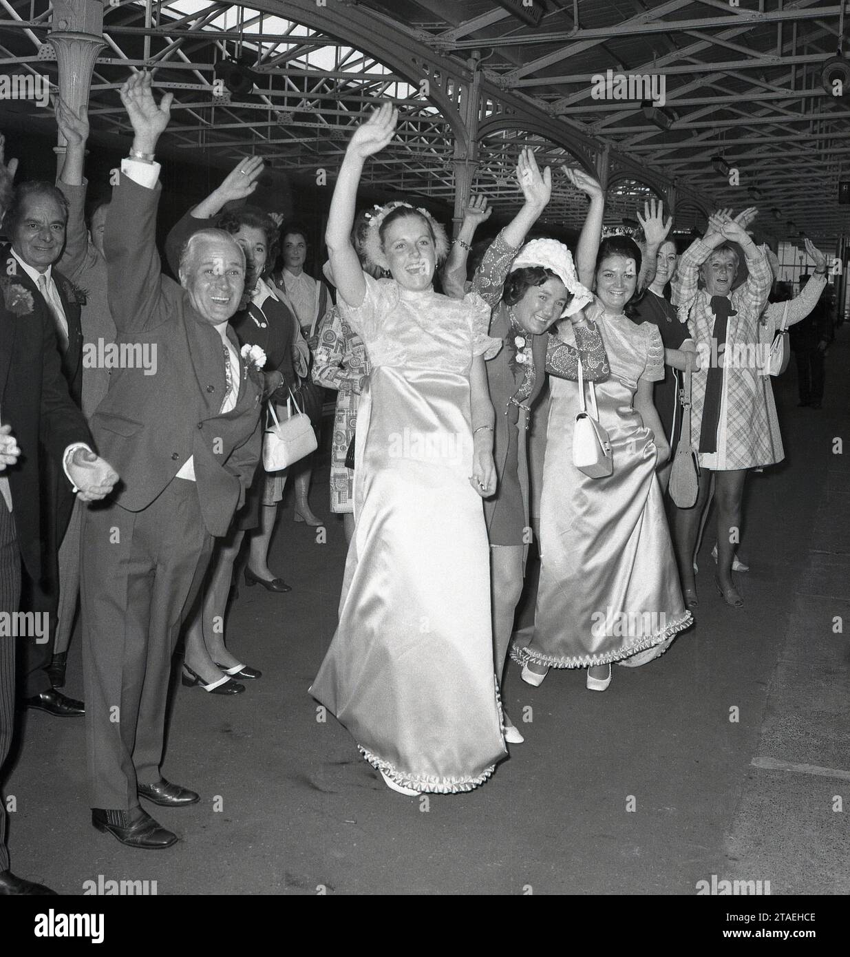 Anni '1960, storico, un gruppo di ospiti di nozze, tra cui damigelle d'onore si riuniscono sul binario di una stazione ferroviaria per dare un grande rimando al coupé appena sposato, Inghilterra, Regno Unito. Foto Stock
