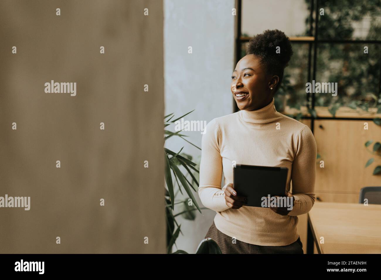 Una bella giovane donna d'affari afroamericana con un tablet digitale a parete in ufficio Foto Stock