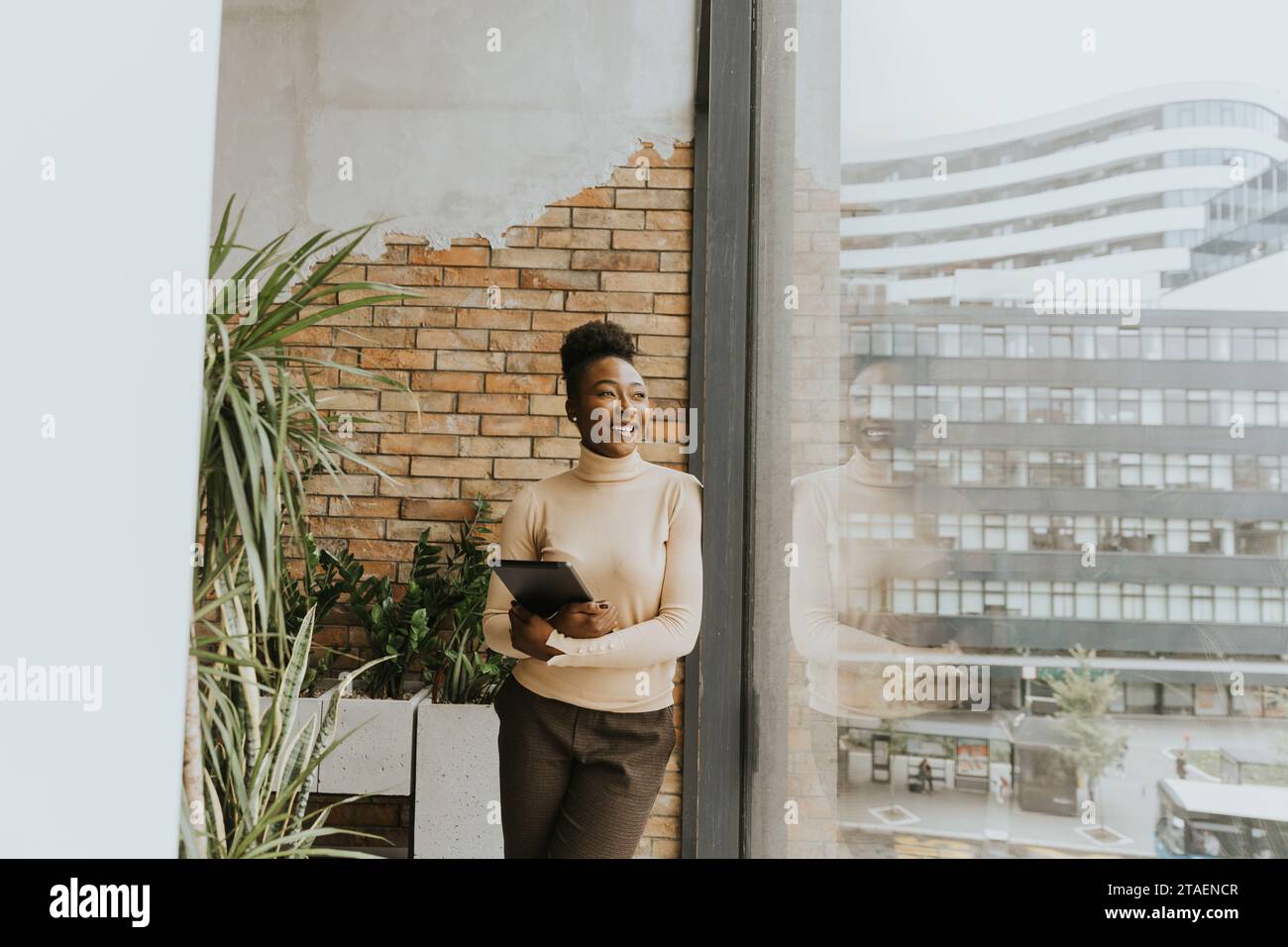 Una bella giovane donna d'affari afroamericana con un tablet digitale in piedi accanto al muro in stile industriale Foto Stock