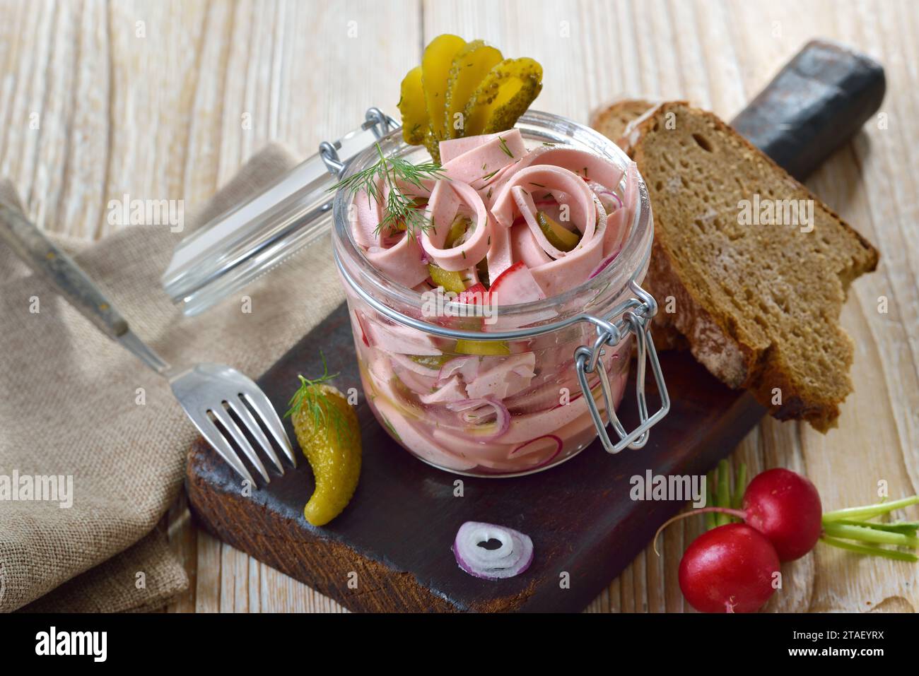 Abbondante insalata di salsiccia bavarese servita in un barattolo di vetro su un vecchio tagliere di legno Foto Stock