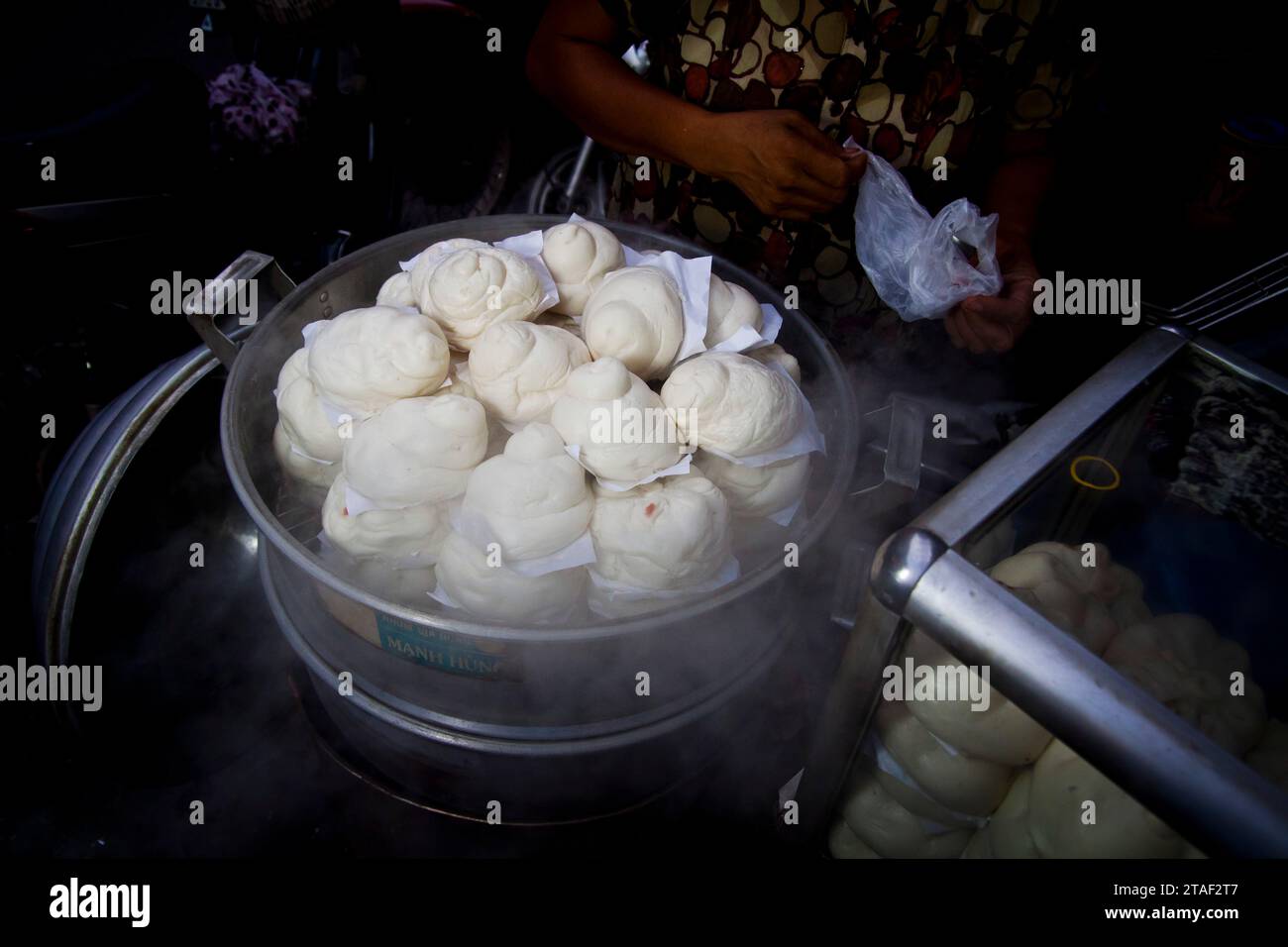 Una donna che vende banh bao (panini al vapore) in una bancarella a bordo strada ad Hanoi, in Vietnam Foto Stock