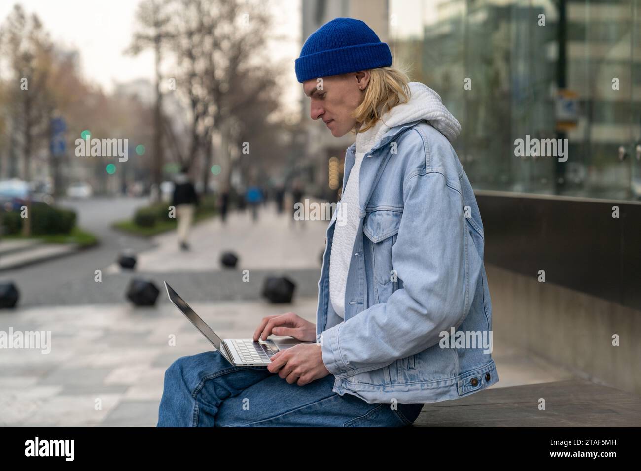 L'uomo concentrato autosufficiente con il laptop si siede vicino all'edificio lavora come programmatore nell'azienda IT Foto Stock